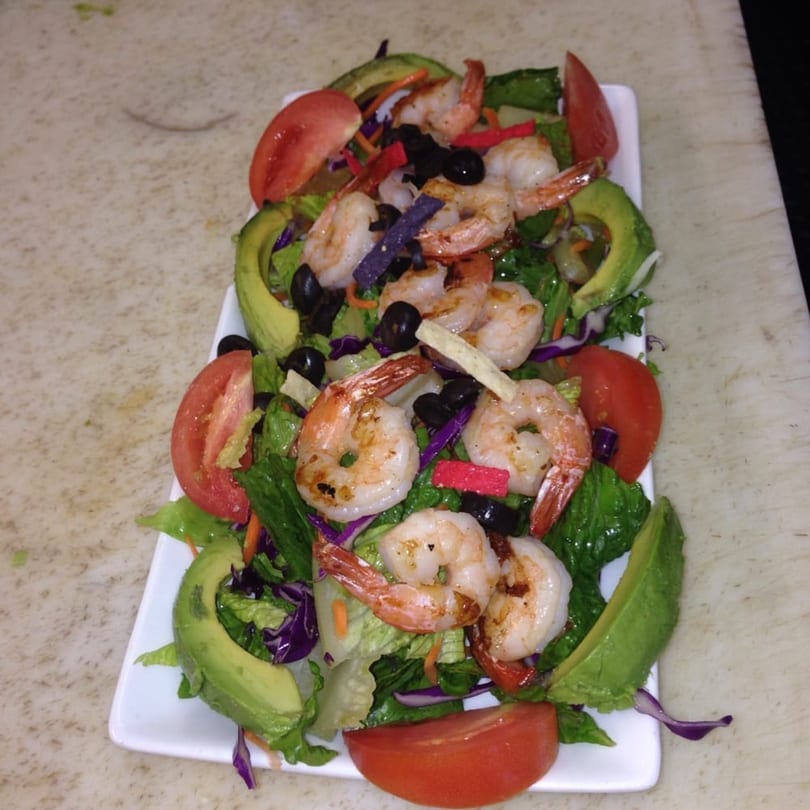 A vibrant Mexican shrimp salad with lettuce, avocado, tomatoes, olives, and tortilla strips.