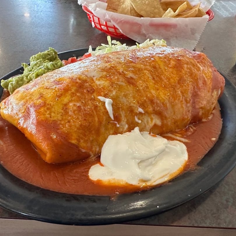 A large, saucy burrito with guacamole, shredded lettuce, and sour cream on a black plate.