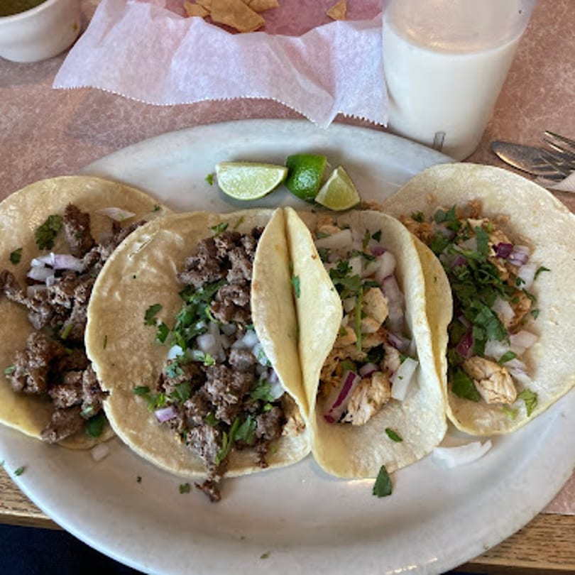 Four Carmela's Mexican Restaurant tacos, two with beef and two with chicken, garnished with cilantro and onions.