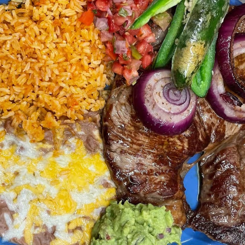 Grilled steak with red onions, rice, refried beans with cheese, guacamole, and pico de gallo.