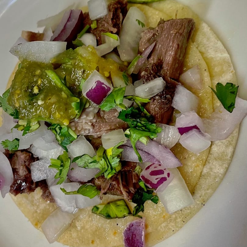 Close-up of a Carmela's Mexican Restaurant taco with meat, green salsa, white and red onions, and cilantro.